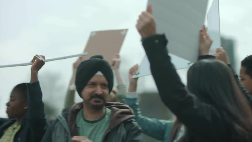 A multicultural group of people smiles and look at each other as they protest in a city