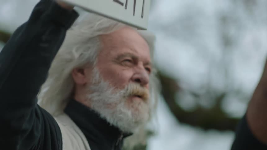 A man is chanting while holding a sign