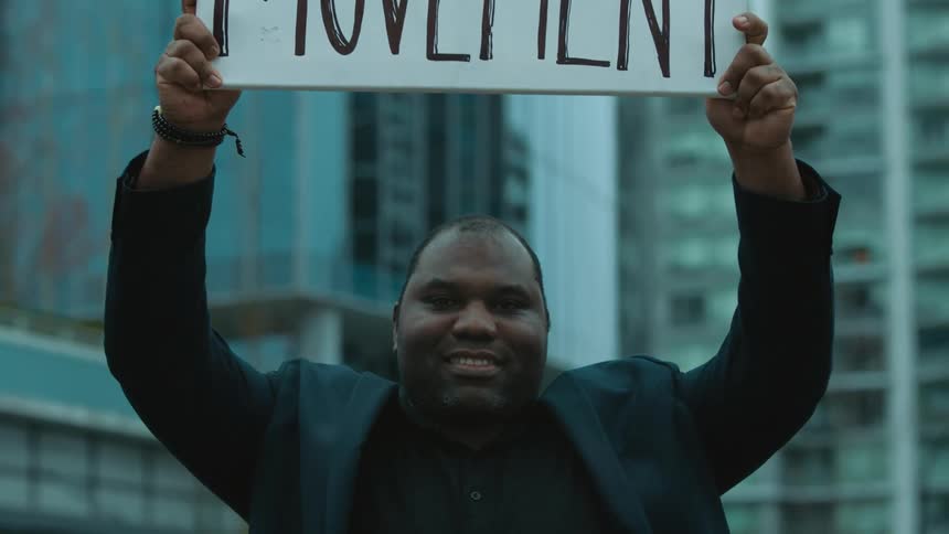 A man is holding up a protest sign in a downtown city
