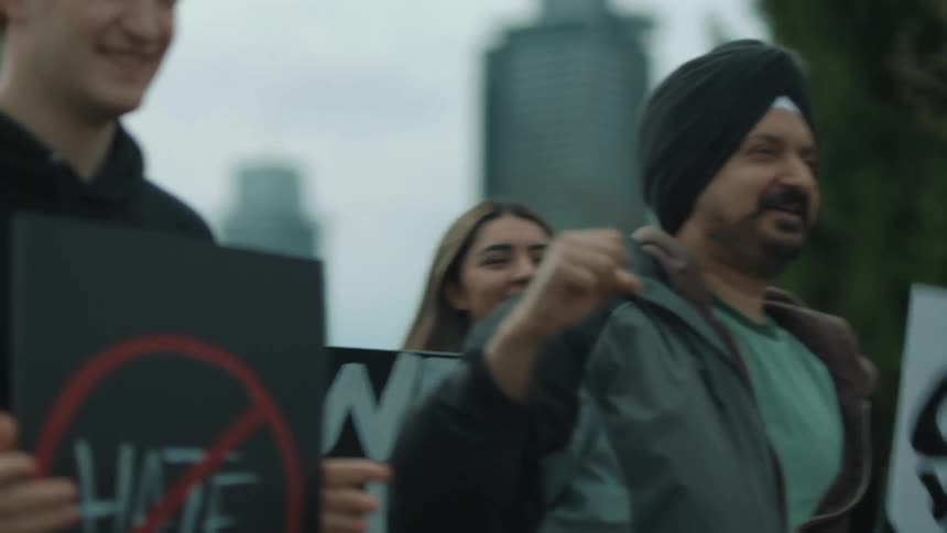 People are in a park raising their fists and chanting as they protest with signs