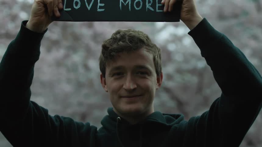 A man smiles as he raises a protest sign