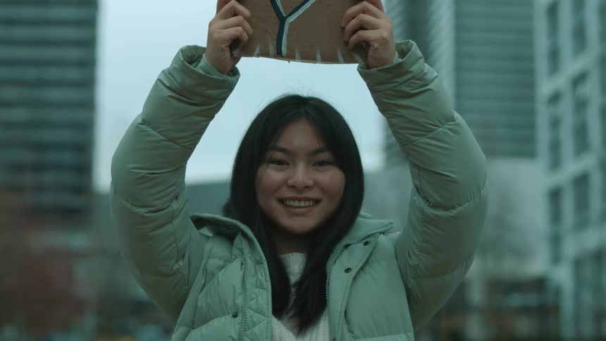 An asian woman is outdoors protesting in a downtown city