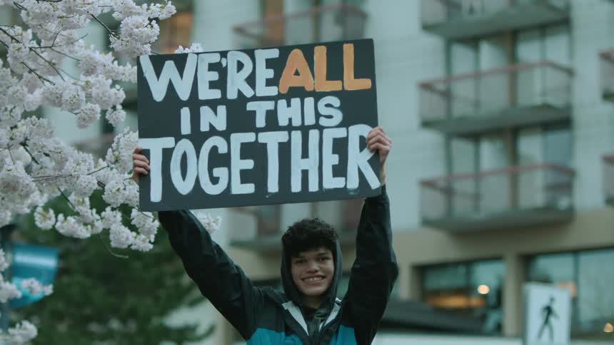 Happy young man standing outdoors in front of a building lifting a placard with an uplifting message