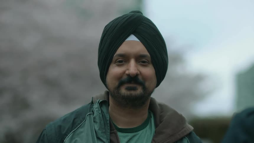 A man smiles into the camera while standing outdoors during the day