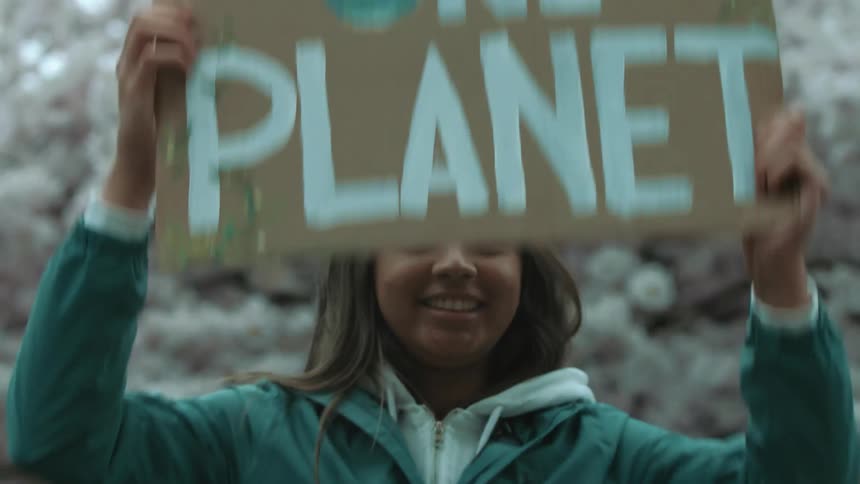 A young Indian woman smiling happily as she raises a sign that says one planet at a rally