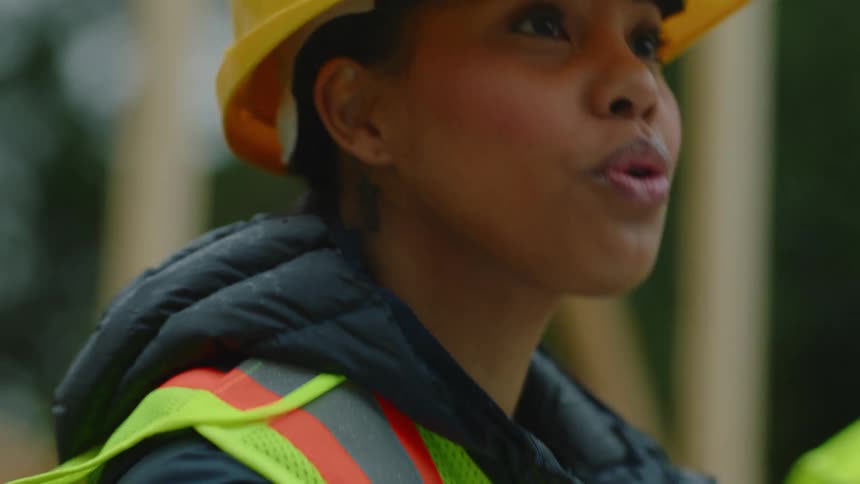 Female construction worker wearing a safety helmet and a vest talking to her coworkers at a construction site