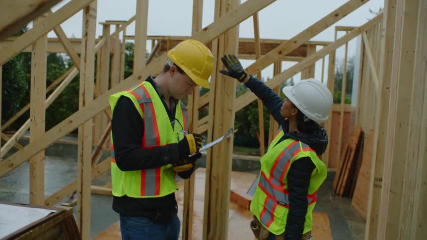 A female construction worker is pointing and giving instructions to her coworker and he is writing on a clipboard