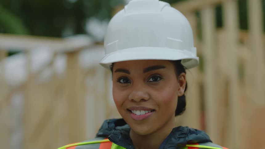 A female construction worker wearing a white hardhat smiles and nods her head