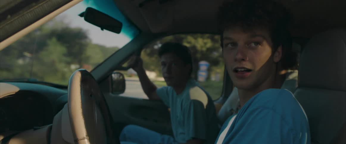 Three excited young men in a car driving through a residential neighborhood on a sunny day
