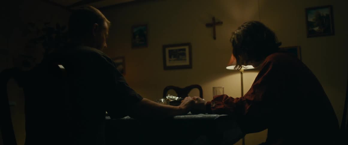 A father and son pray together before eating a meal at a table in a home dining room