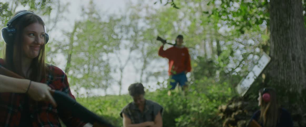 A girl smiles as she shoots a gun in a forest while her friends watch
