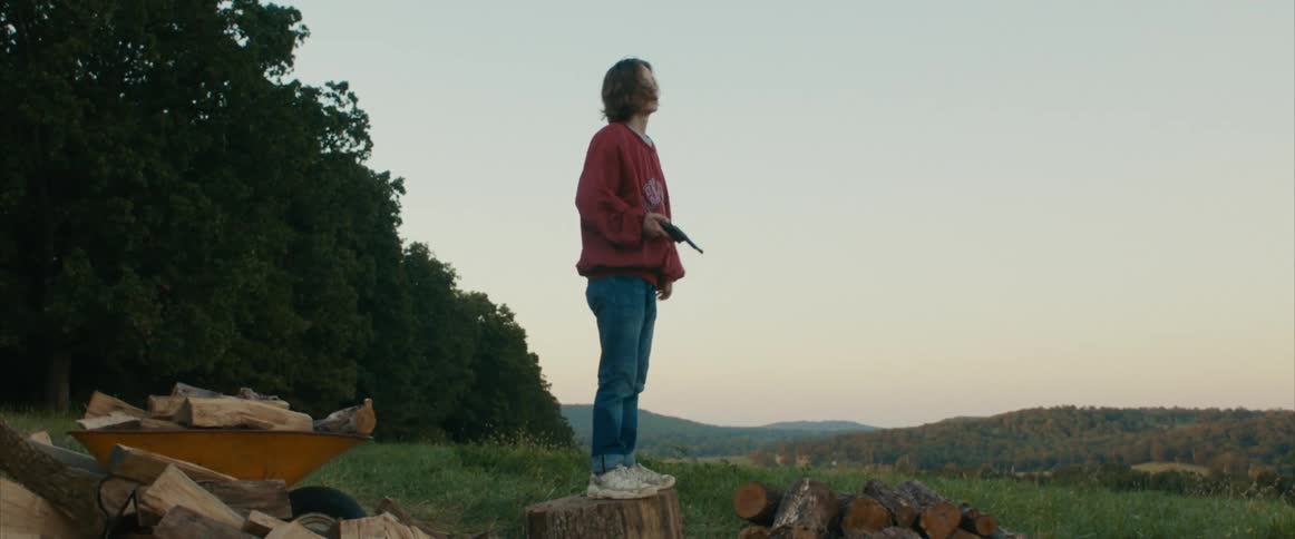 A young man is standing outside holding a gun then he raises it