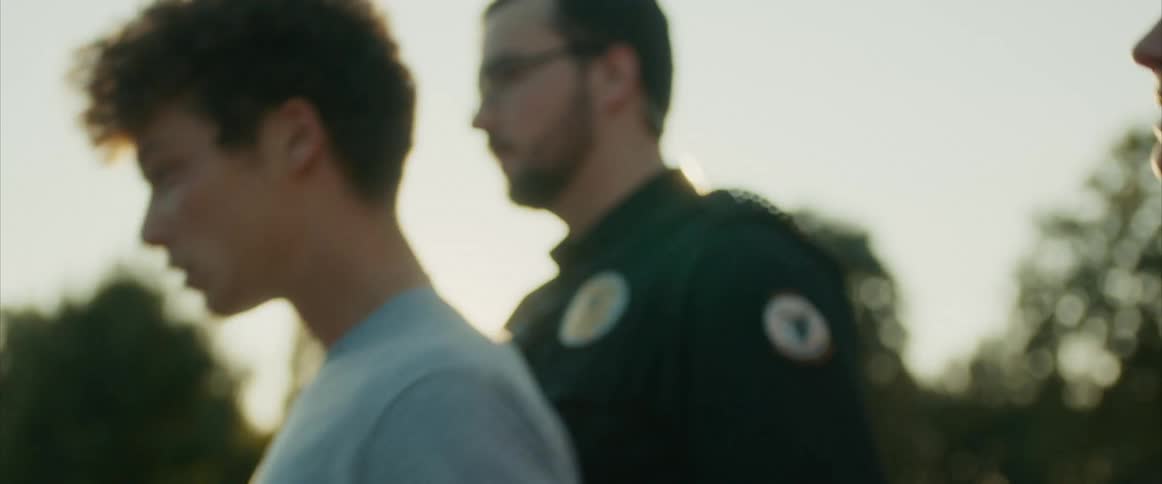 A cop leads a teenager in handcuffs to a car as the mother follows and cries