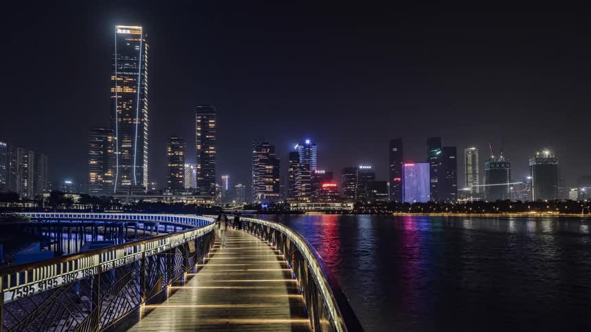 Time lapse of people walking across a bridge with a lit up city skyline in the distance