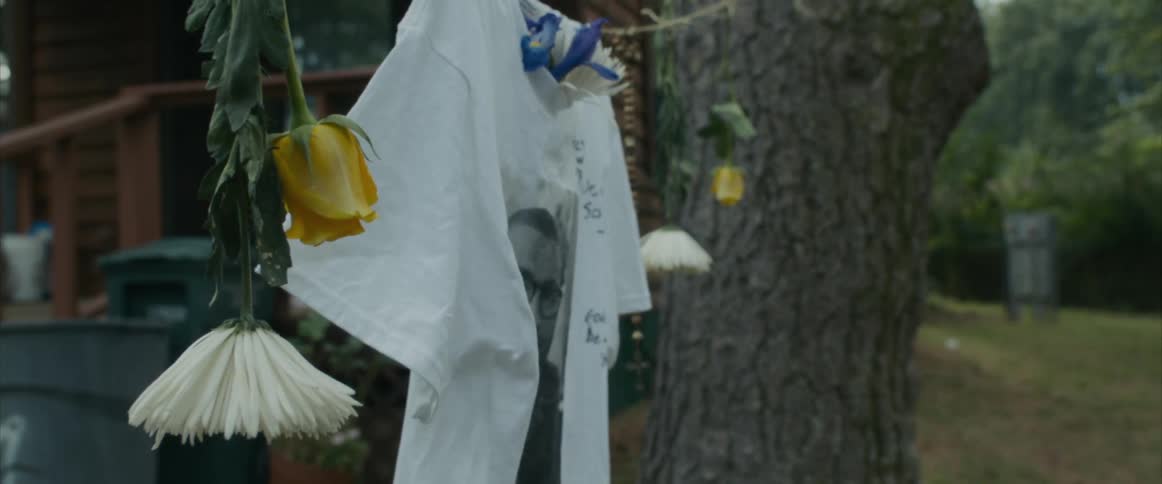 A memorial shirt is hanging by a tree outside of a house