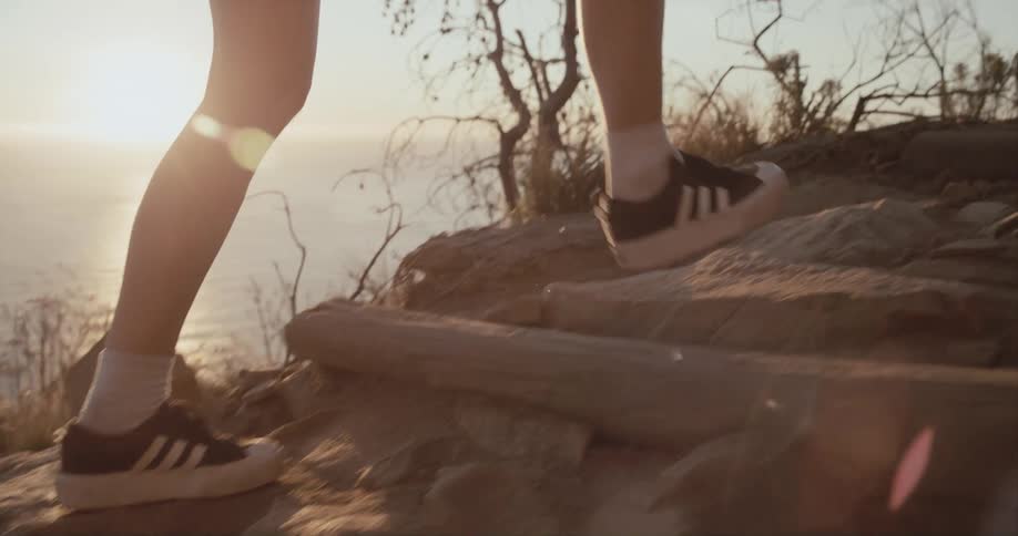 A woman wearing shorts walks up a hill with makeshift steps overlooking the ocean
