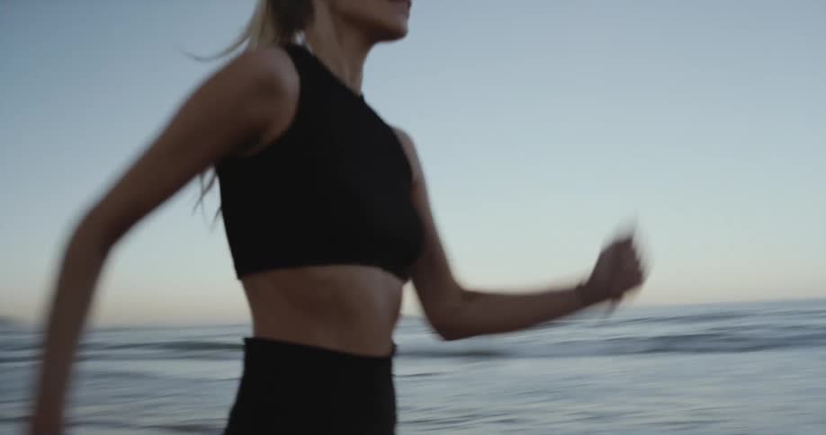 Blonde woman jogs across beach toward figure standing still near houses on shore