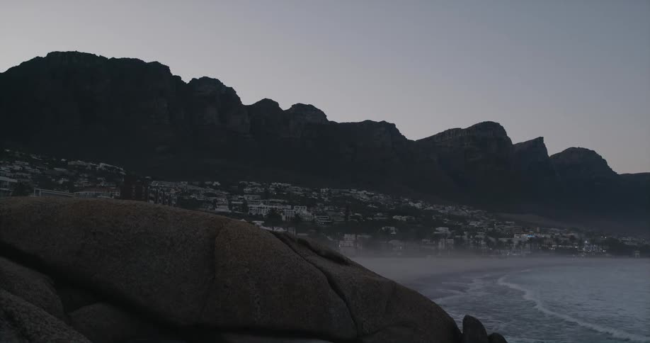 A mountain ridge looms over a small town on the coast in the evening