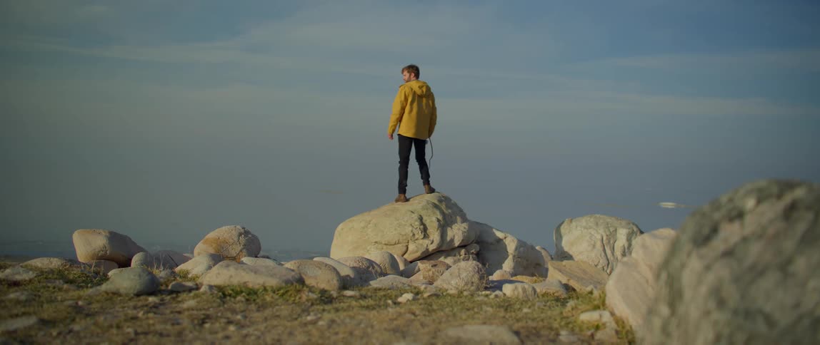 A man walks to the rocky cliff and takes pictures of the water in front of him