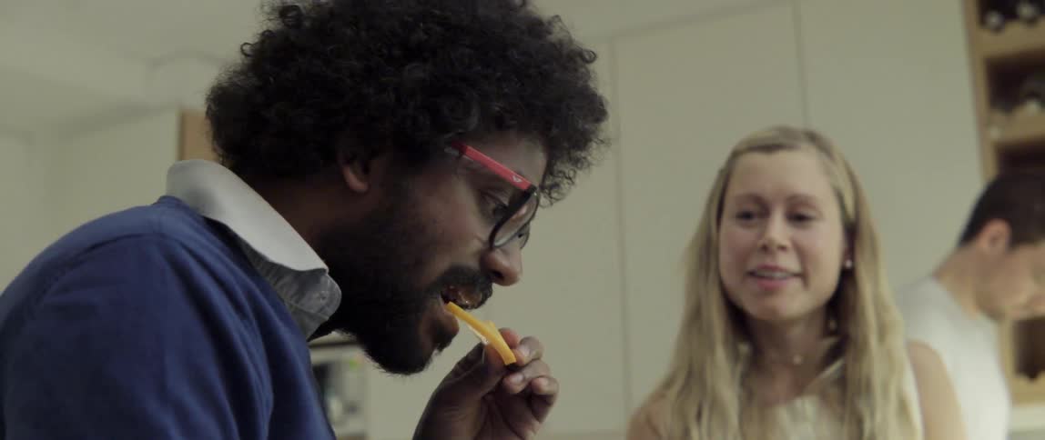 Man Eating Food While Others Watch With Warm Encouragement and Shared Mealtime Connection