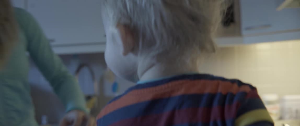 A toddler mixes something in a bowl and is helped by his mother