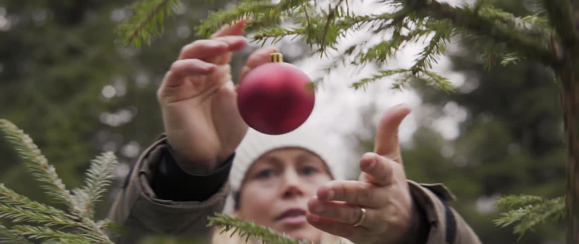 Woman hanging ornament from outdoor tree branch with warm joyful holiday feel