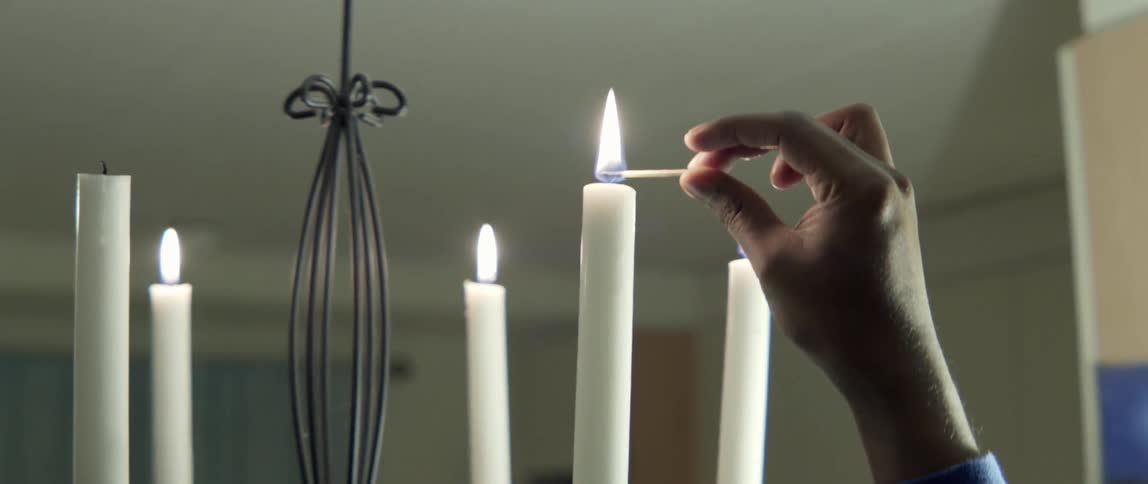 Match lighting candles in chandelier casting warm glowing light with intimate atmosphere.