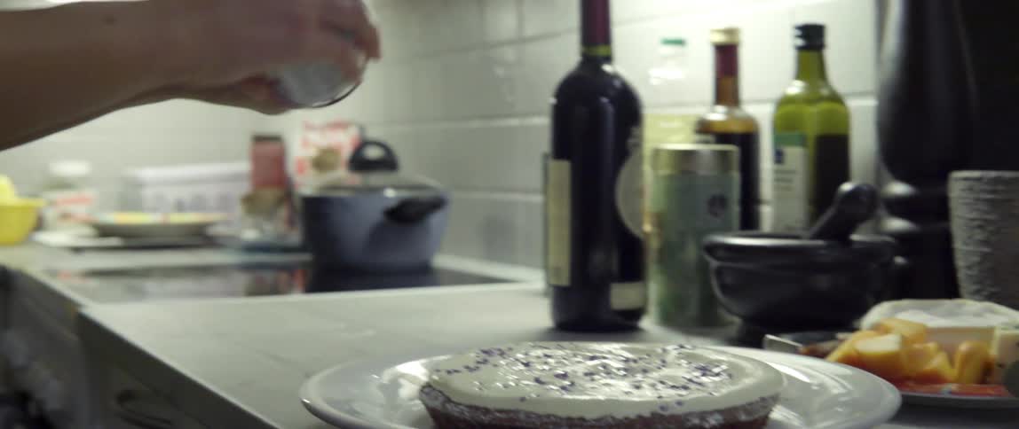 Woman Joyfully Scattering Sprinkles Over a Frosted Dessert With Playful Care in the Kitchen.