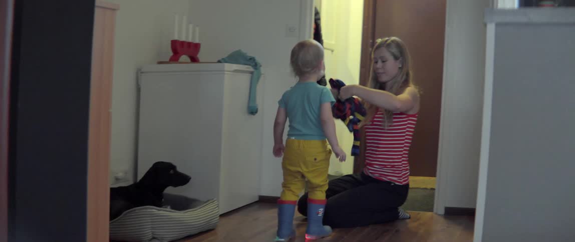 Young woman helping a small child put on winter clothing in a modern house.