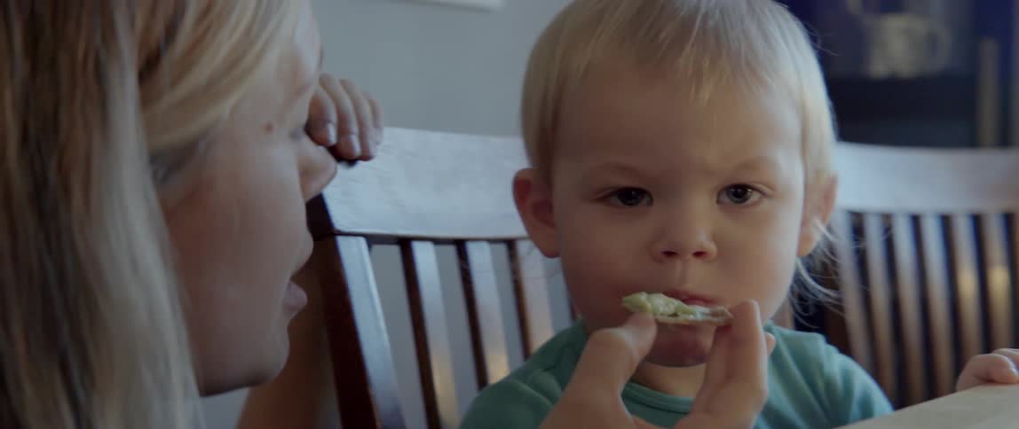 A woman feeds a cracker with something on it to a toddler