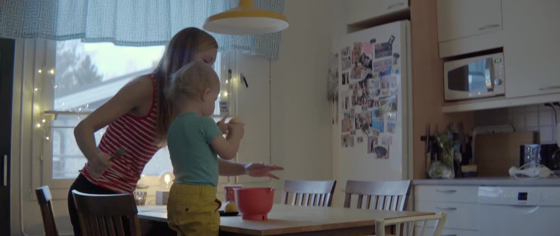 A mother and her young son mix ingredients together in a bright modern kitchen.
