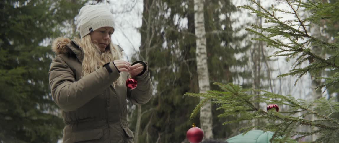 Woman holding ornament next to outdoor tree with warm joyful holiday spirit