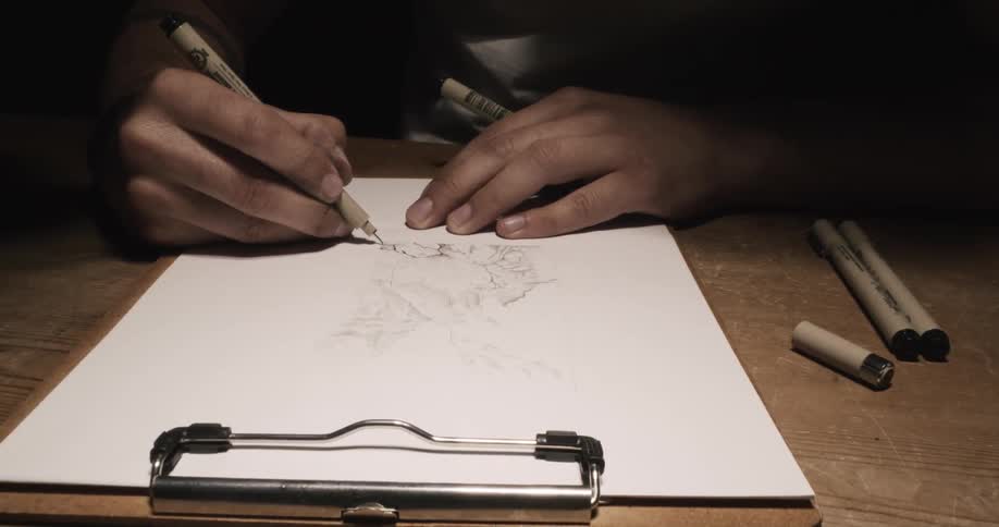 A man sits at a table and sketches