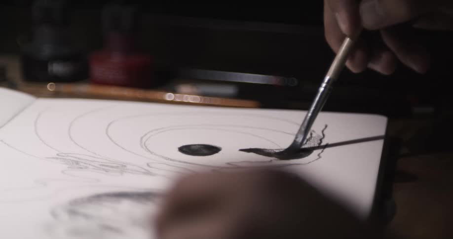 An artist uses black watercolor to fill in a sketch