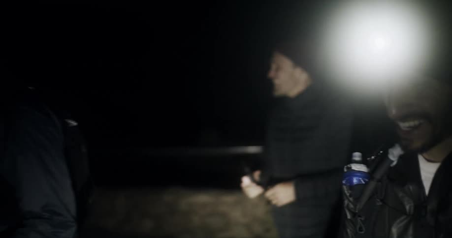 A group of men hike through a public park while wearing headlamps at night
