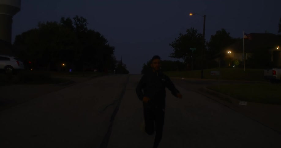 A man jogs along a street through a residential neighborhood as the sun begins to rise