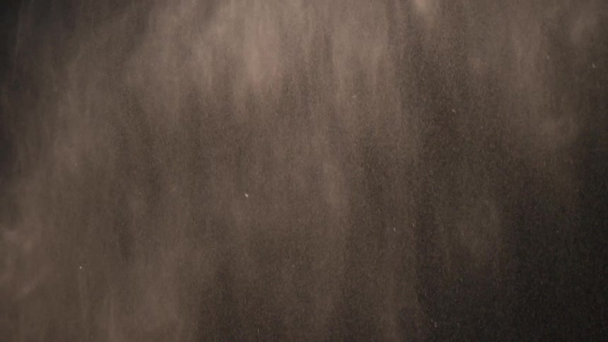 Pale powder falls through air in darkness