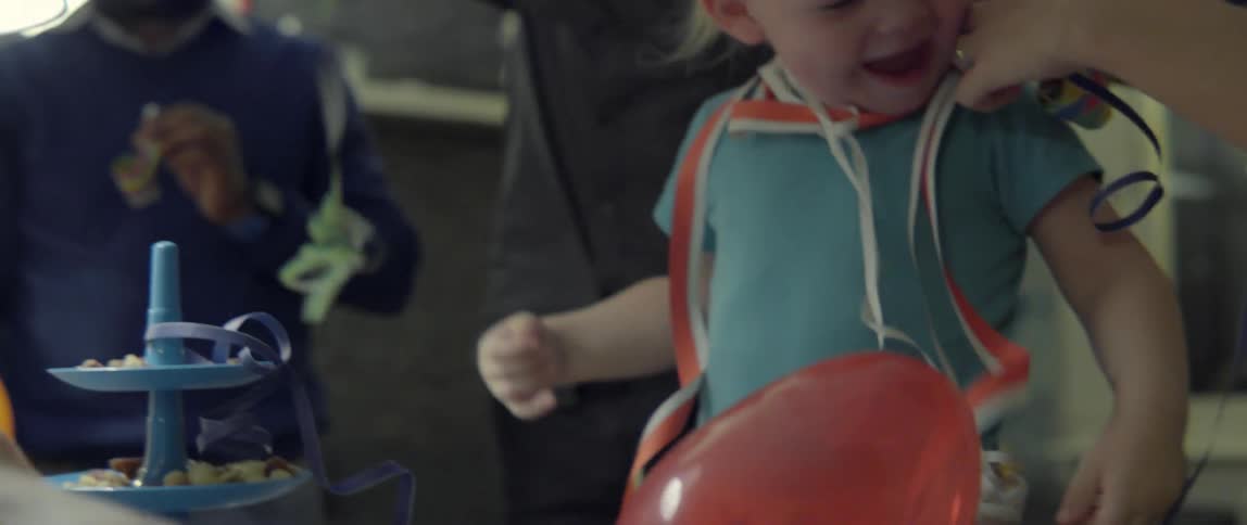 A man plays with colorful party streamers while a laughing toddler enjoys the celebration.