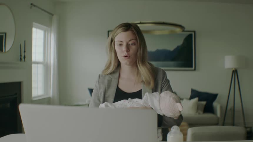 A woman holds her baby while on a video call on her laptop
