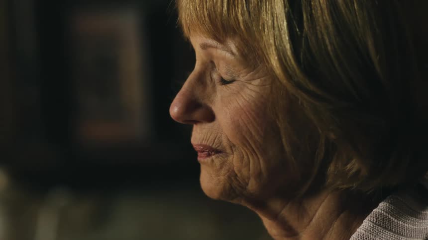 A woman touches her cheek and sighs while standing in the kitchen