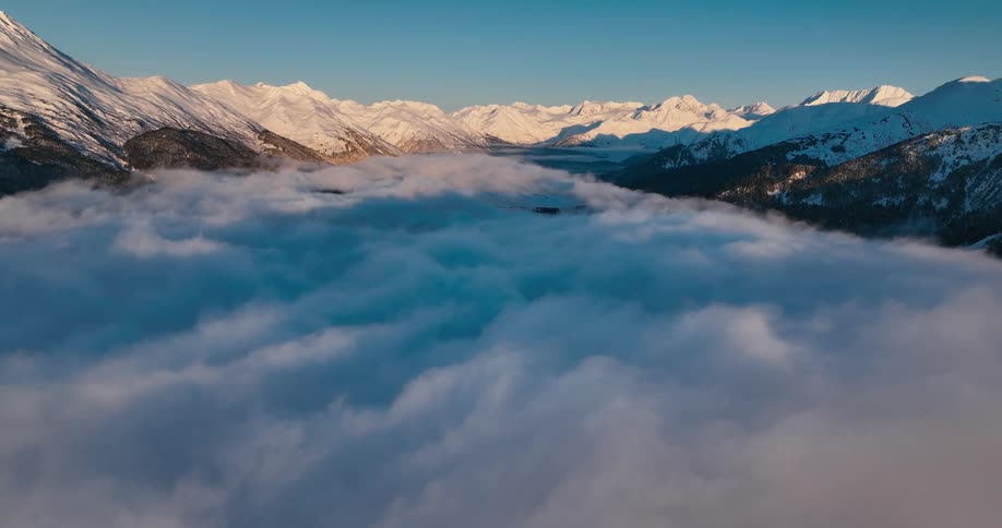 Snow covered mountain summits tower over low lying clouds