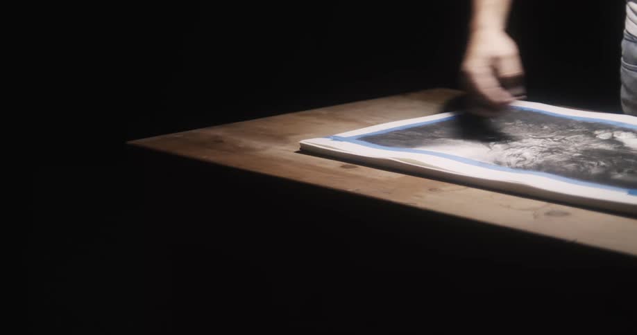 A man uses charcoal to color on a sketch on paper