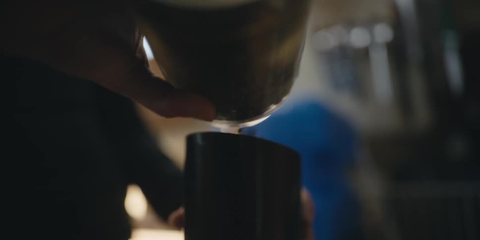 A person pouring coffee beans in a black coffee mug