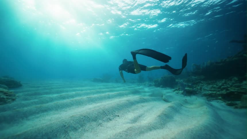 A diver swims underwater near the sea floor during the day