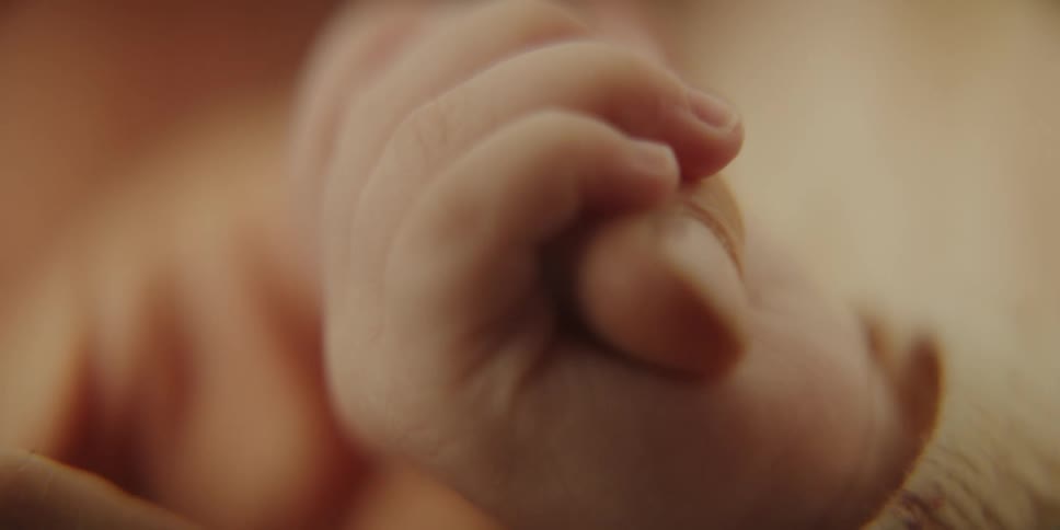 A baby clasps the forefinger of an adult