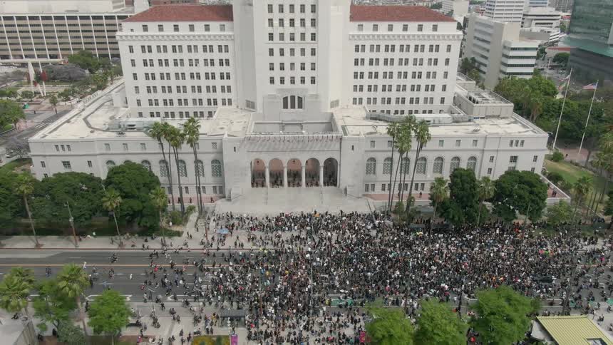 A large crowd of people is protesting outside a building in a city