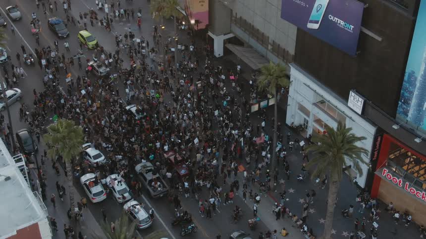 A group of protesters crowd the road and sidewalk outside a building during the day