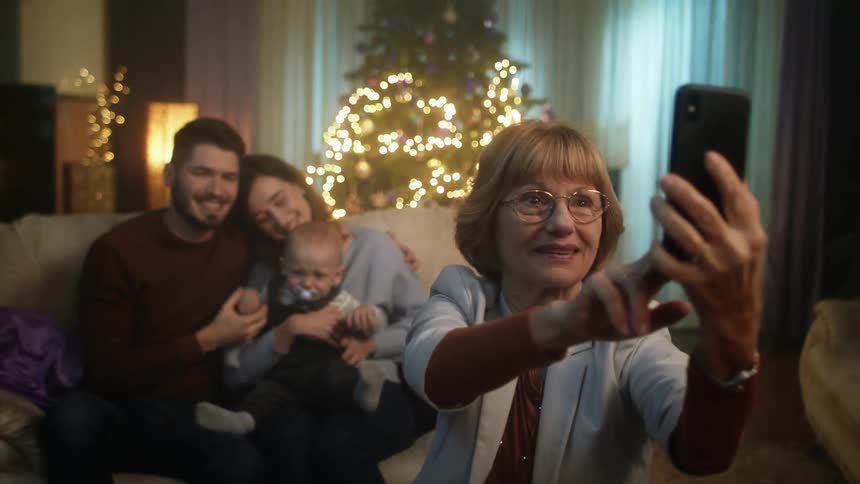 A grandmother holds up a cell phone to take a selfie with her adult children and grandchild behind her