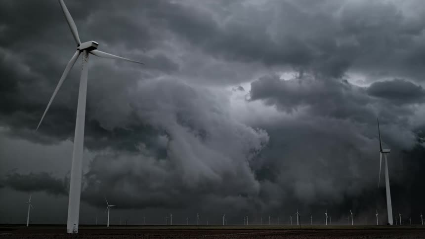 Wind turbines spin on a wind farm under a dark stormy sky