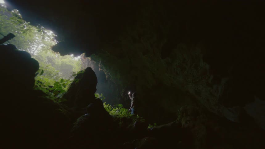 A man standing in a cavern raises his smartphone to photograph the opening of the cave